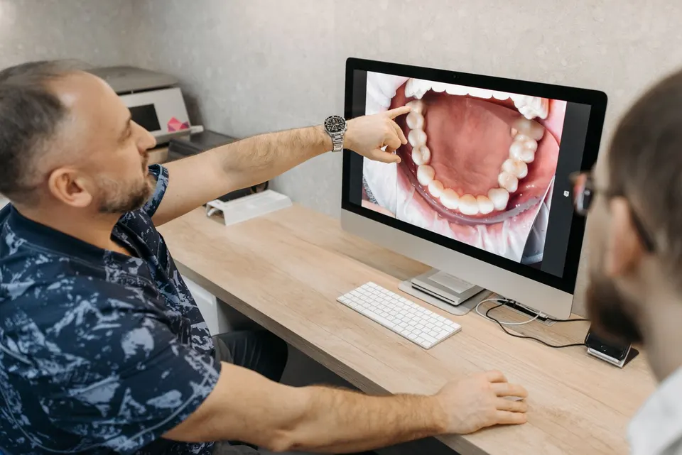 Dentiste pointant l'image numérique d'une arcade dentaire inférieure sur un écran d'ordinateur